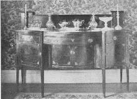 A fine old Hepplewhite sideboard, with old glass and  silver, but the modern wallpaper is not in harmony.