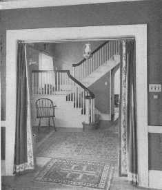 This attractive Colonial hallway shows a good arrangement of rugs. The border on the portières spoils the effect, but the lamp is well chosen.