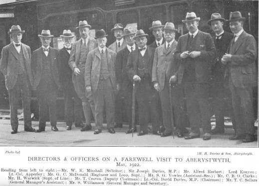 Directors & Offices on a Farewell Visit to Aberystwyth, May 1922.  Reading from left to right:—Mr. W. K. Minshall (Solicitor); Sir Joseph Davies, M.P.; Mr. Alfred Herbert; Lord Kenyon; Lt.-Col. Apperley; Mr. G. C. McDonald (Engineer and Loco. Supt.); Mr. S. G. Vowles (Assistant-Sec.); Mr. C. B. O. Clarke; Mr. H. Warwick (Supt. of Line); Mr. T. Craven (Deputy Chairman); Lt.-Col. David Davies, M. P. (Chairman); Mr. T. C. Sellars (General Manager’s Assistant); Mr. S. Williamson (General Manager and Secretary).  Photo by H. H. Davies & Son, Aberystwyth