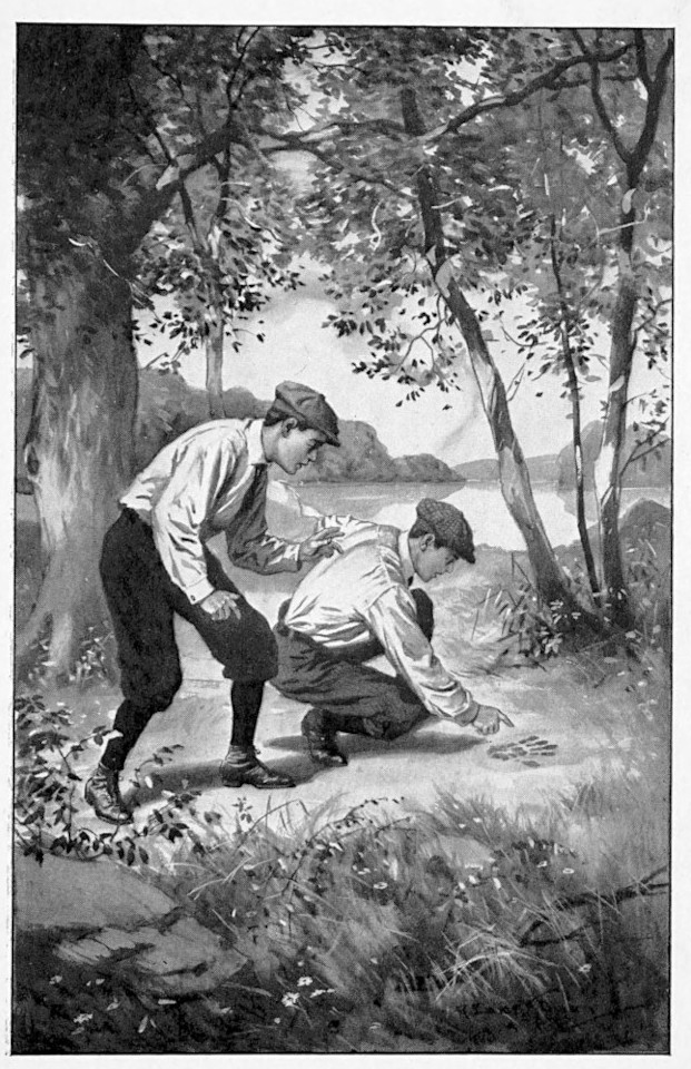 Two boys crouched looking at a footprint.