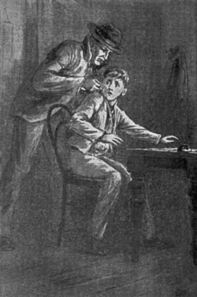 A boy sits at a table in a darkened room. An older man, wearing a suit and hat, holds the boy firmly by the ear.