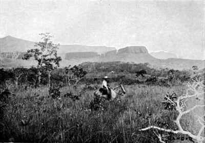 Quadrangular Rocky Mountain connected by Natural Wall of Rock with the Vertical-sided Range in Background.