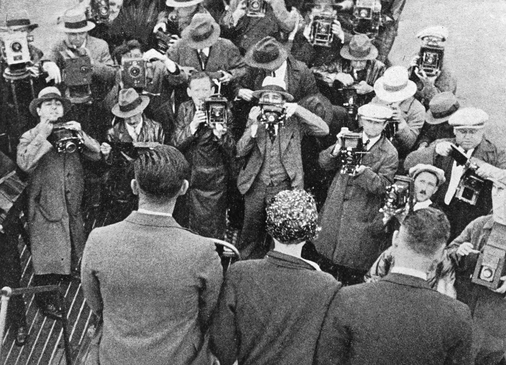 Photo high over shoulder shot of crew facing crowd of photographers