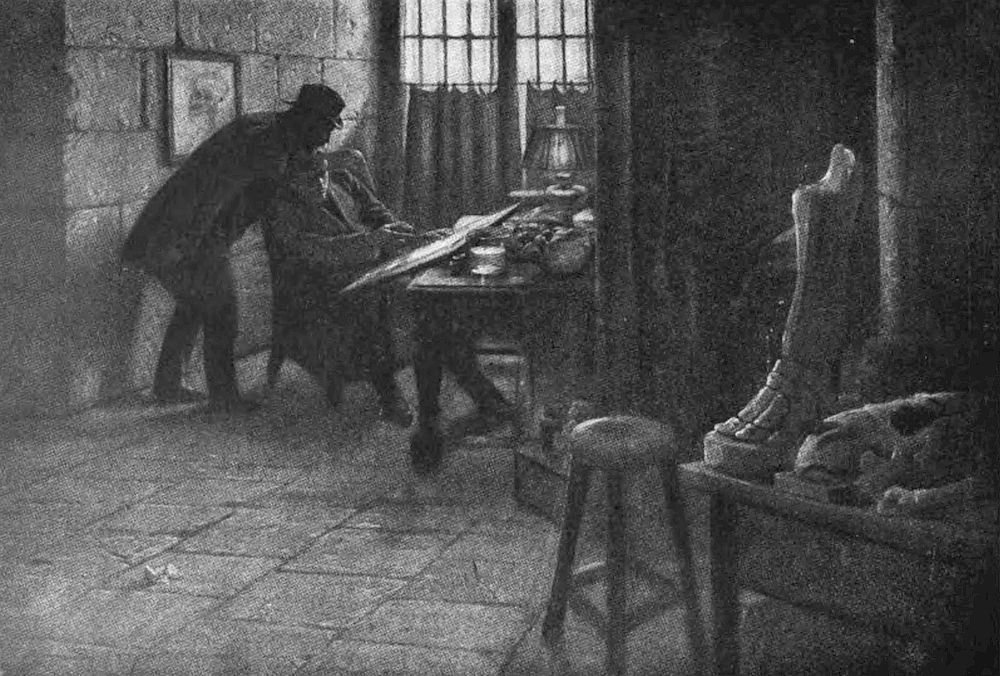 A dimly lit room with stone walls, likely an artist's studio or workshop is showed where a man is seated at a table, intently focused on a drawing in front of him. Another man, wearing a hat and coat, appearing to observe on the artwork.